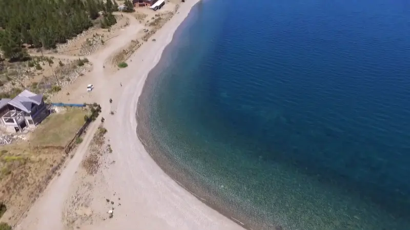 Una playa larga de canto rodado junto al agua azul del Nahuel Huapi, vista desde el aire